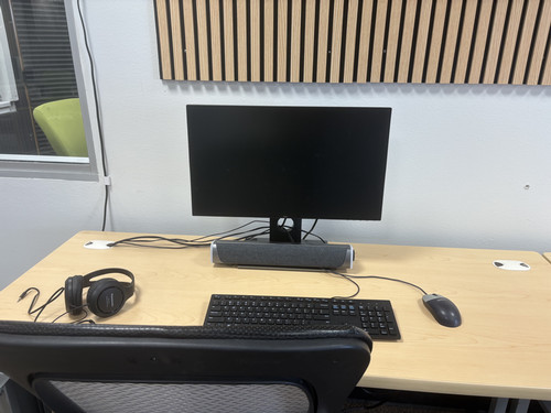 A workspace featuring a computer monitor, keyboard, mouse, and headphones on a wooden desk.